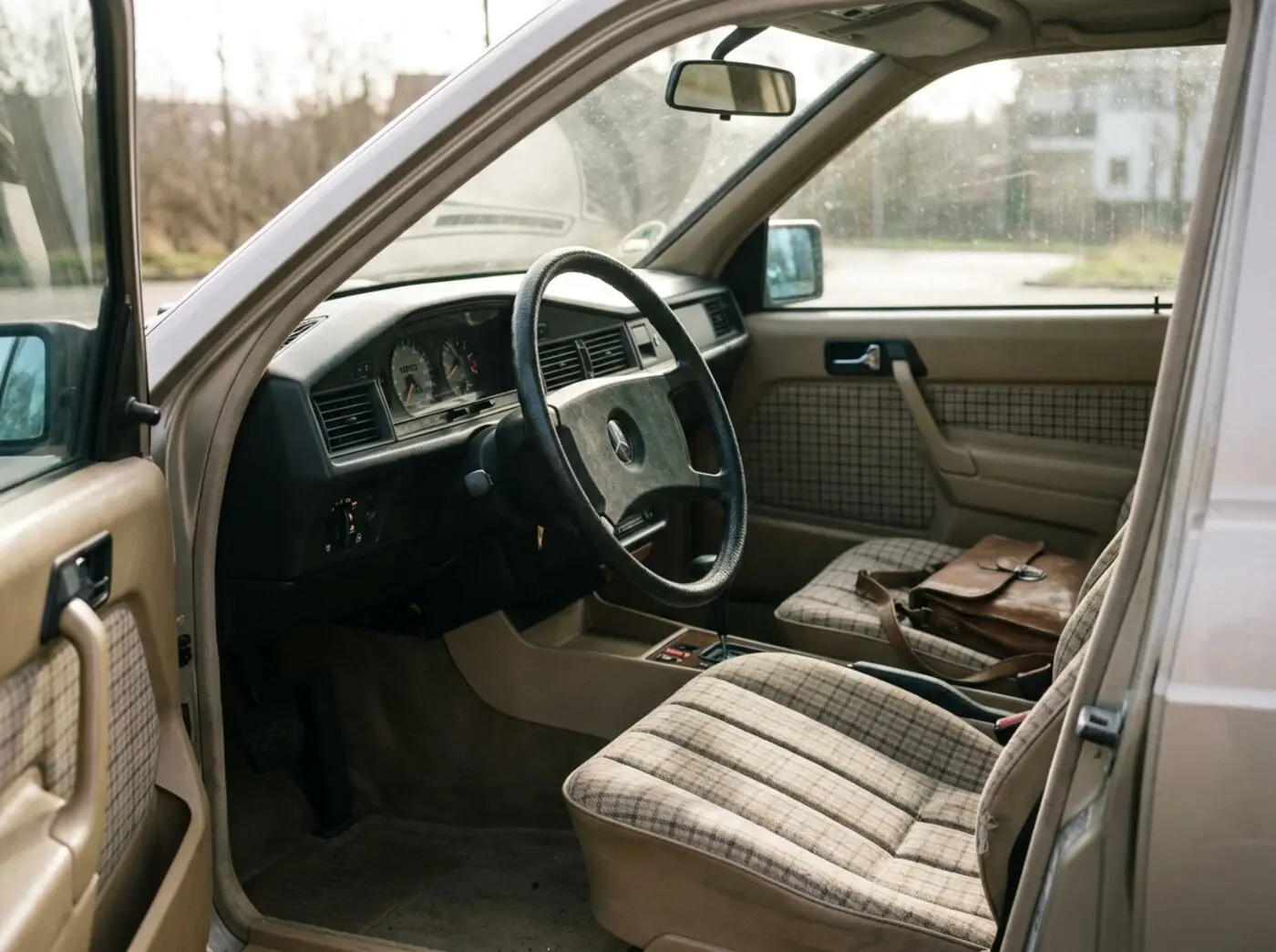 Intérieur Mercedes 190E : sièges en tissu à carreaux, grand volant fin et planche de bord sobre