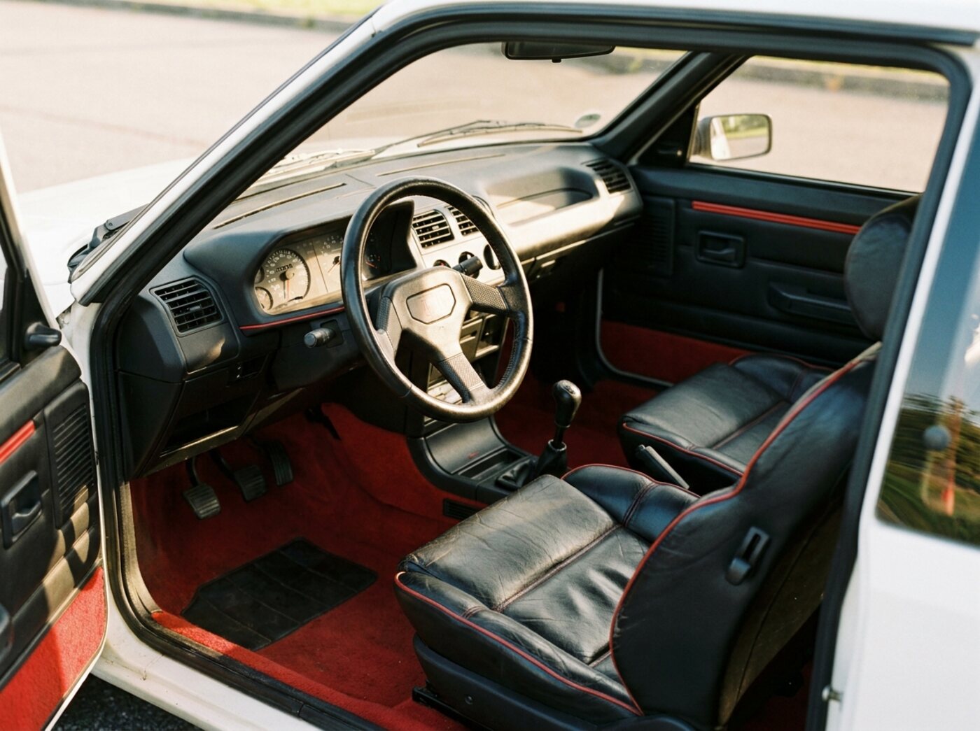 Intérieur Peugeot 205 GTI : sièges semi-cuir à passepoil rouge, moquette rouge, petit volant trois branches